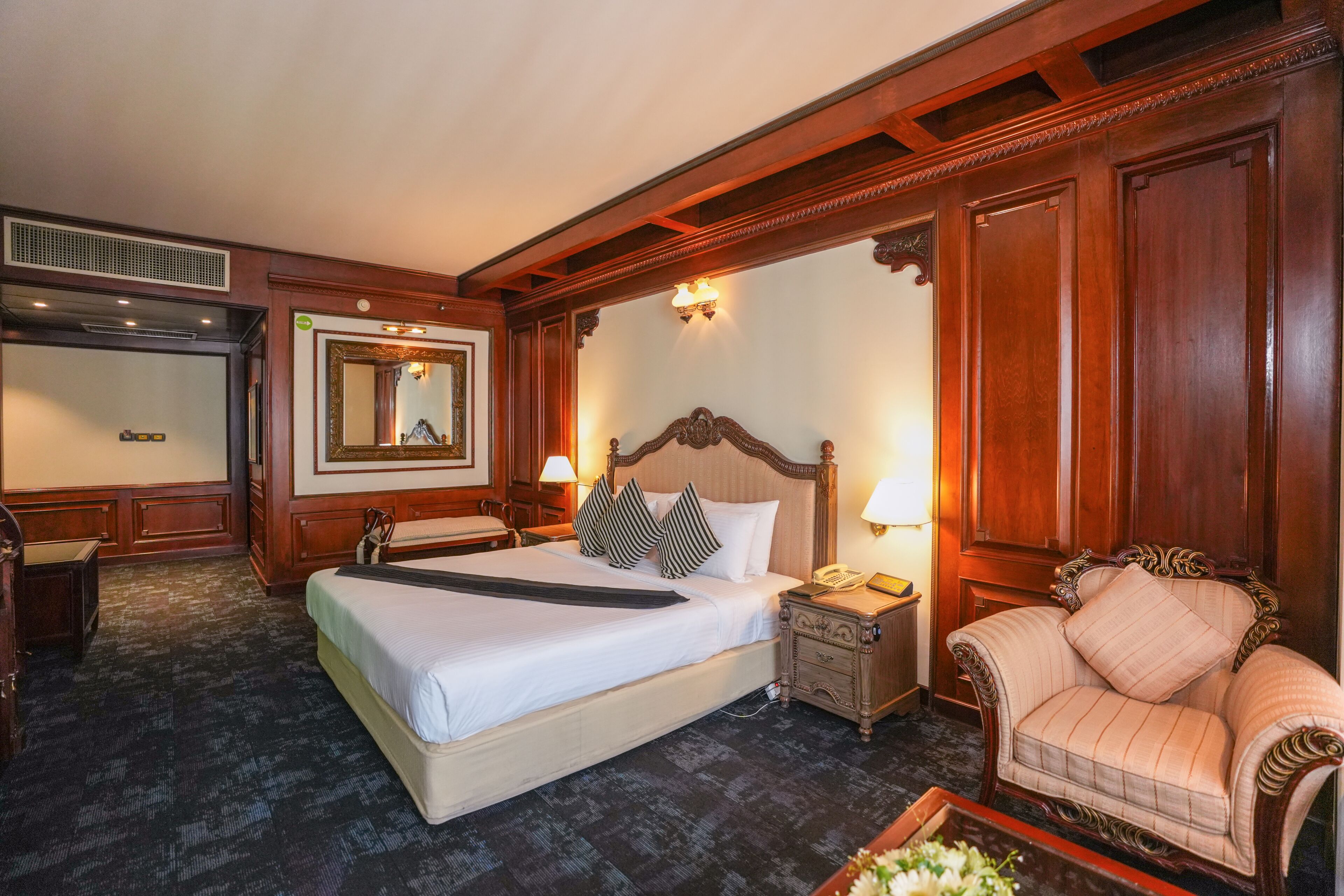 Une chambre d’hôtel avec un grand lit, une table de chevet, une chaise, un miroir et une lampe fixée au mur.