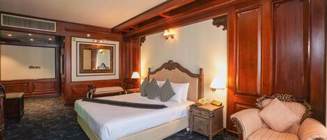 A hotel room with a large bed, a nightstand, a chair, a mirror, and a wall-mounted lamp.