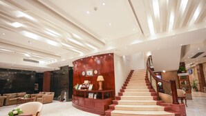 Un vestíbulo amplio con un mostrador de recepción curvo, una escalera y un área de descanso con sofás y una mesa de centro.