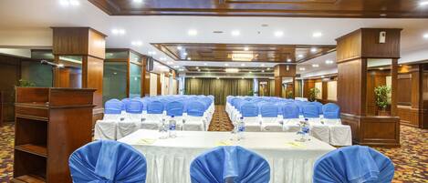 Un salón de conferencias con filas de mesas, fundas azules para las sillas y un candelabro.