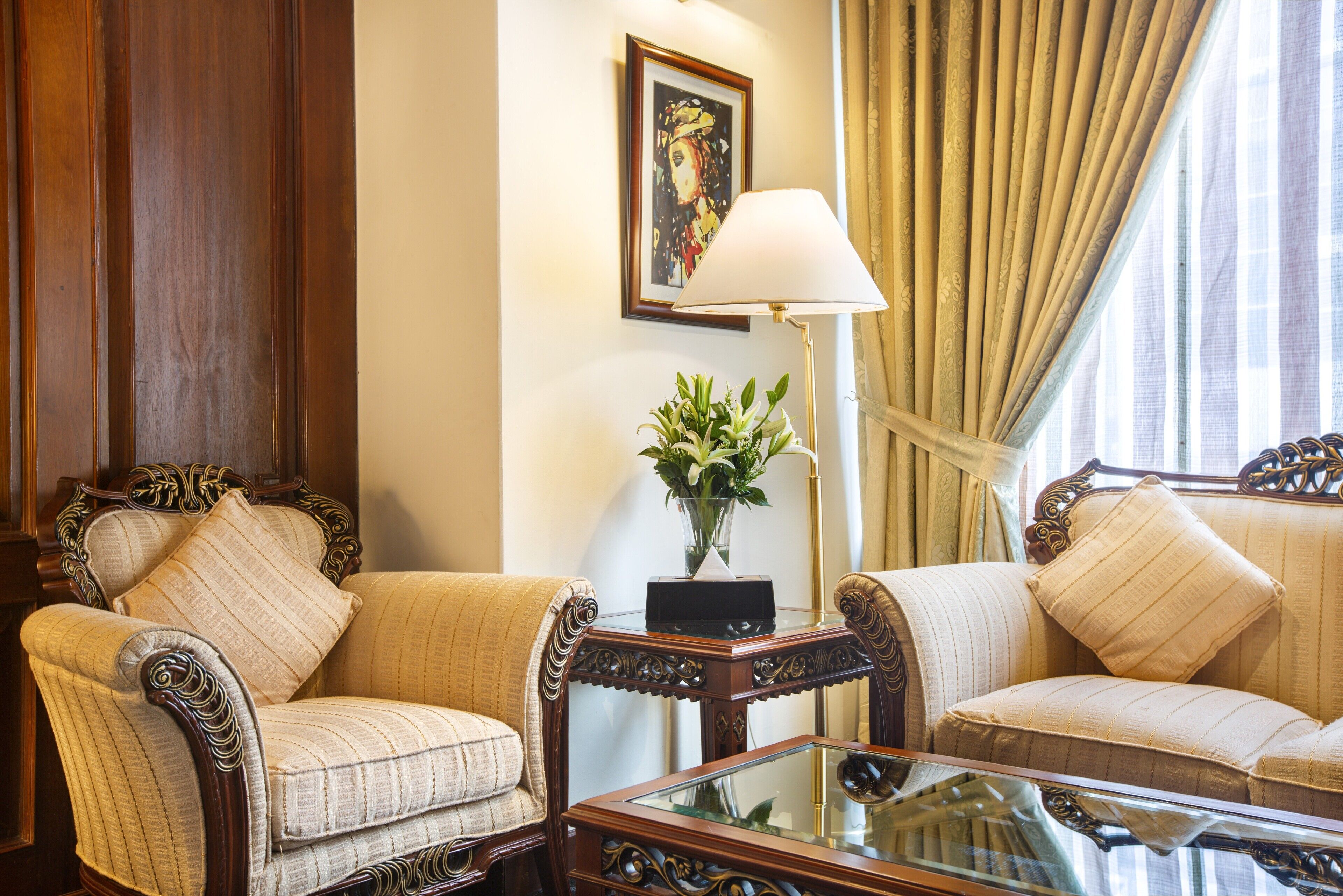 A room with two upholstered chairs, a glass coffee table, a side table with a lamp, and a framed picture on the wall.