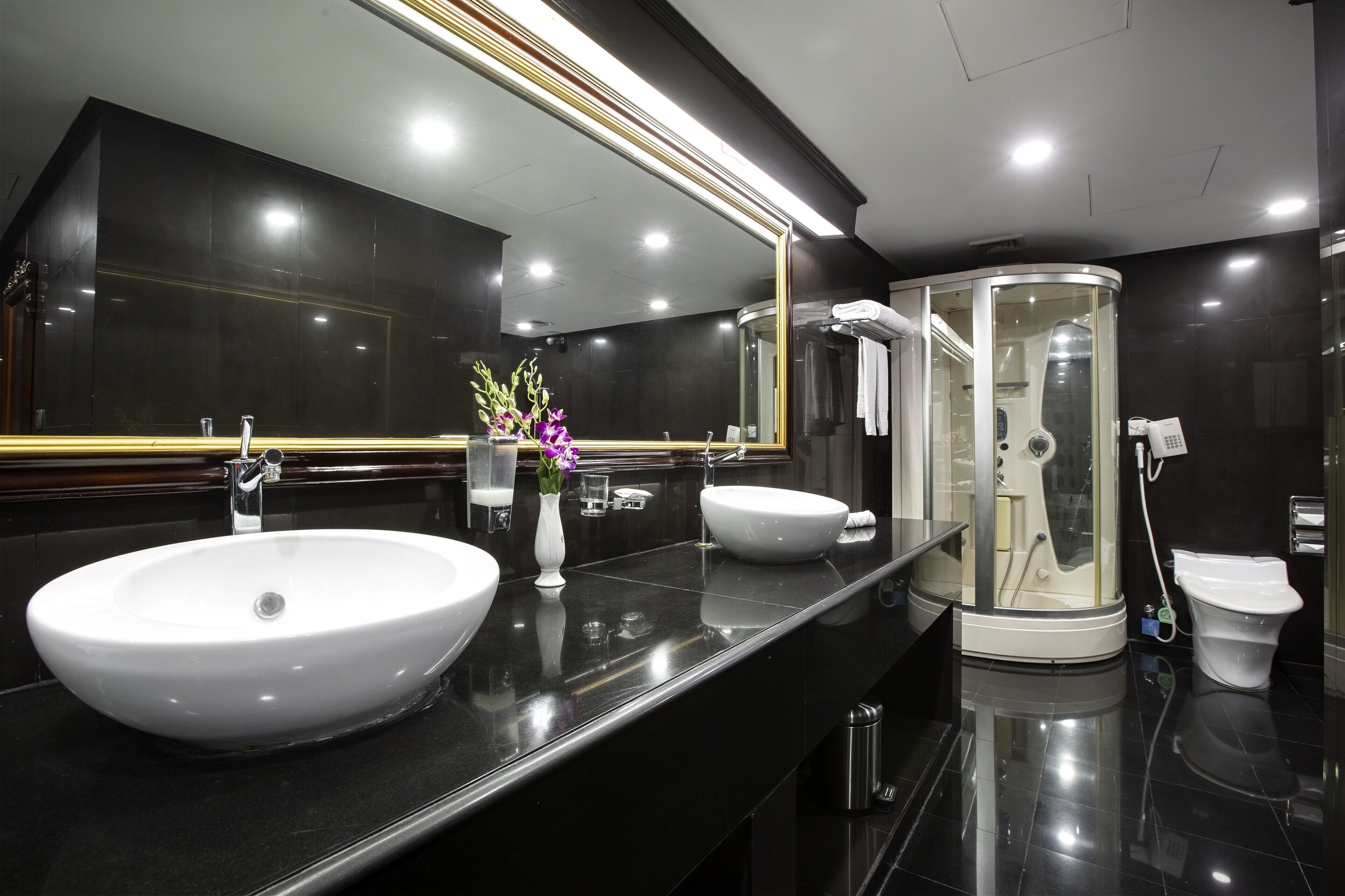 A modern bathroom with two sinks, a large mirror, a glass-enclosed shower, and a toilet.