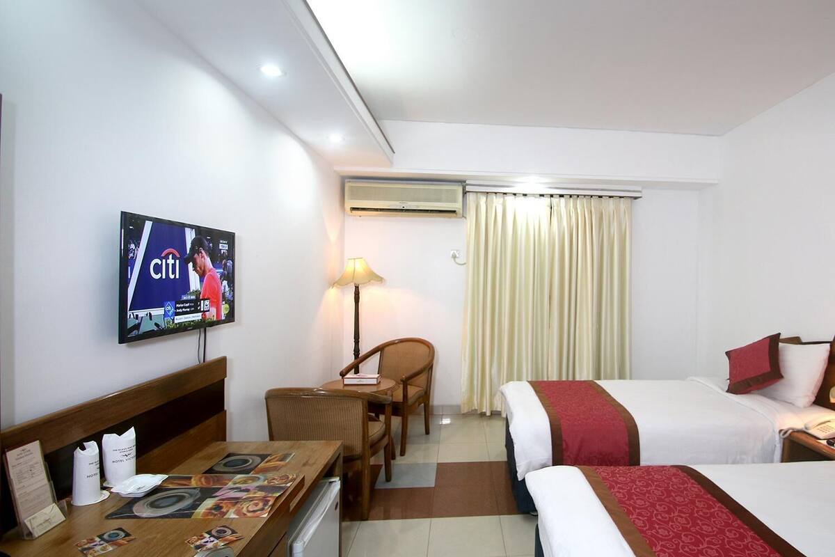 A hotel room with two beds, a desk with a computer, a TV, and a window with curtains.