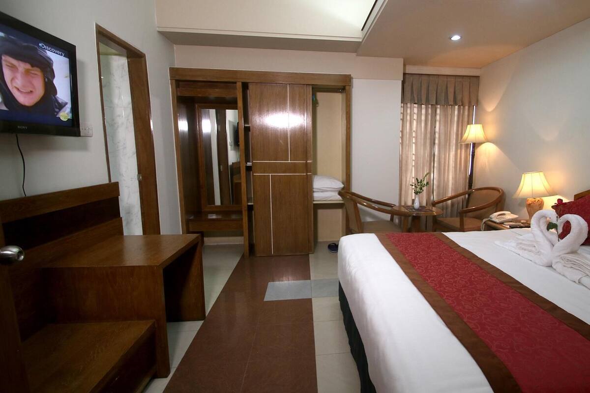 A hotel room with a bed, a desk, a chair, a TV, and a bathroom visible through an open door.