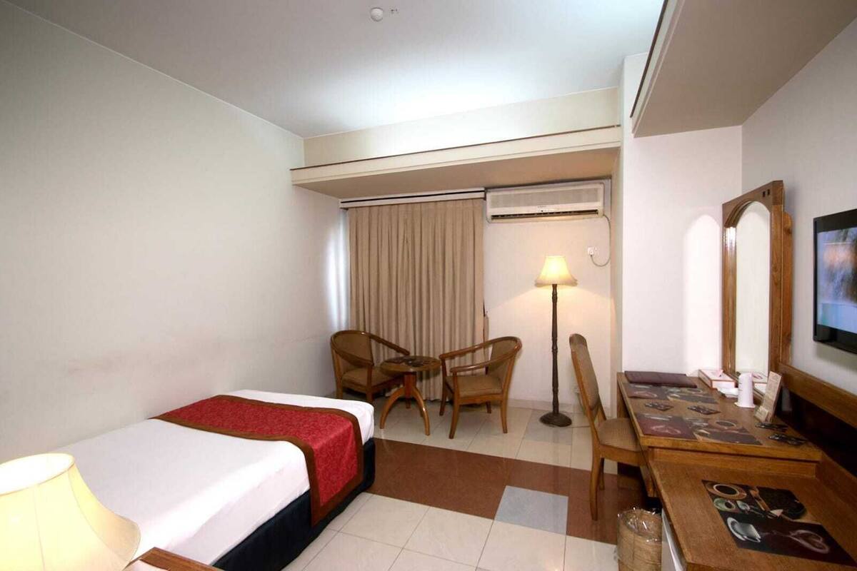 A hotel room with a bed, two chairs, a desk, a lamp, and a TV.
