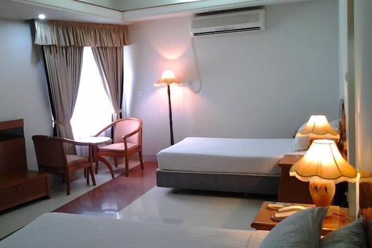 A hotel room with a bed, a desk, a chair, a television, and a lamp.