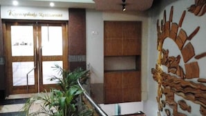 A reception area with a sign reading "Karnaphuli Restaurant" above a double door, a staircase with a handrail, and a wall with a decorative wood carving. - Hotel Victory (Dhaka)
