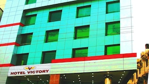 A hotel building with a prominent blue glass facade, a red and yellow lower section, and a sign reading "HOTEL VICTORY". - Hotel Victory (Dhaka)