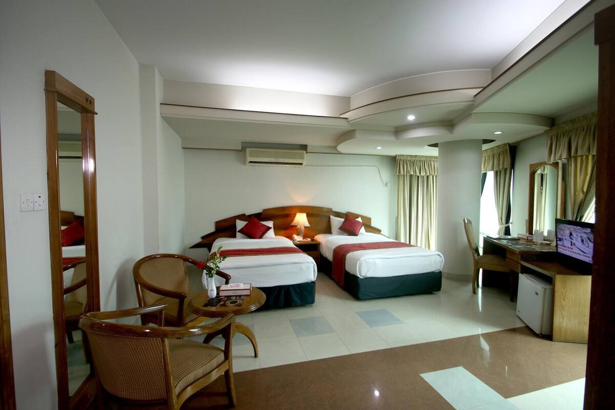 A hotel room with two beds, a desk, a chair, and a television.