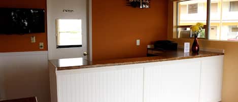 A reception area with a white counter, a 'No Smoking' sign, a 'SOVANA INN' sign, and a window with a view of the outside.