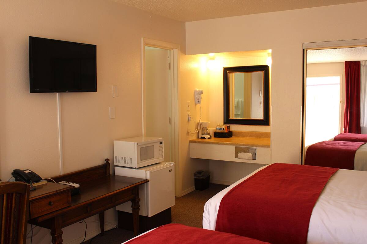 A hotel room with a bed, a desk with a telephone and a microwave, a TV mounted on the wall, and a mirror above the mirror.