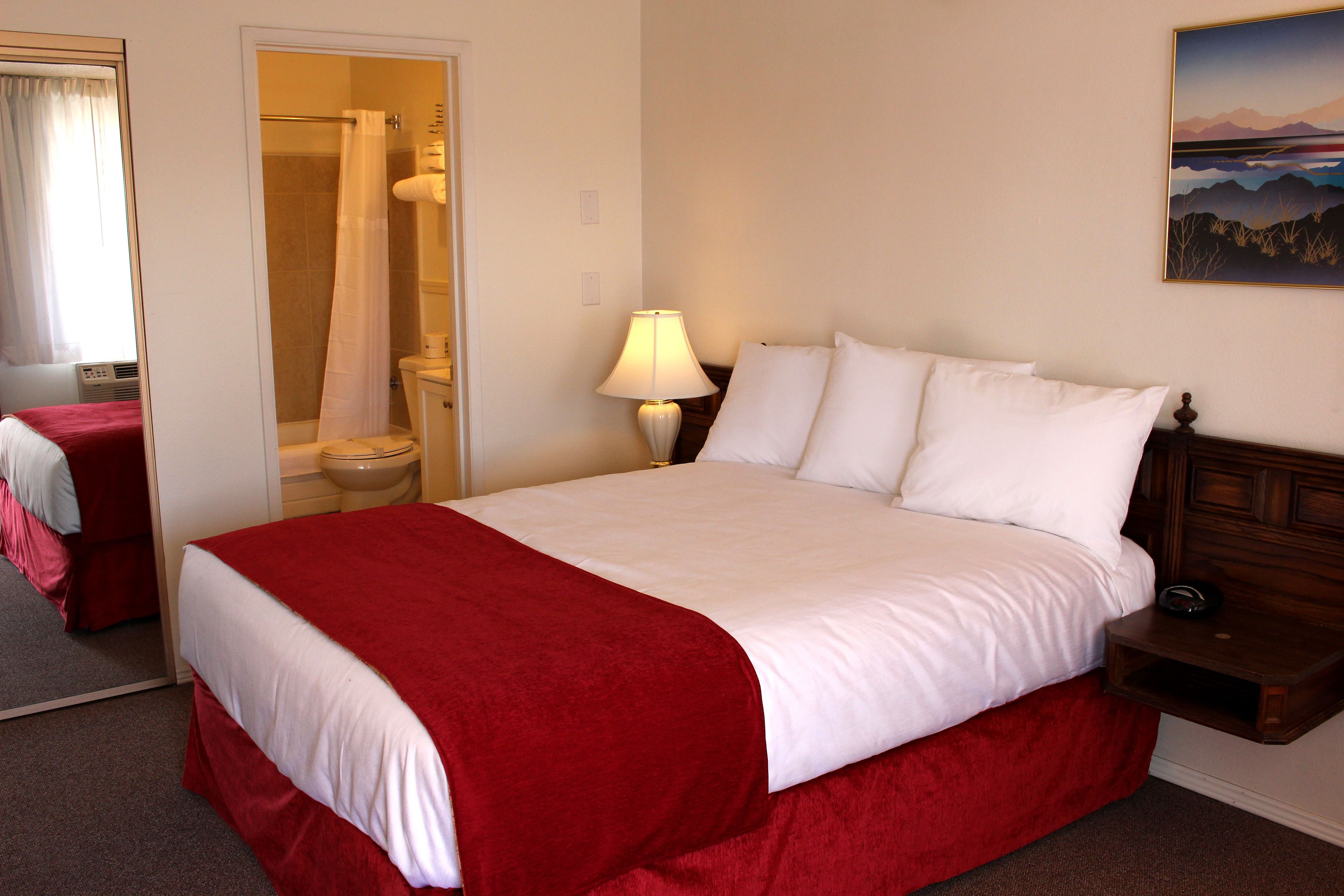 A hotel room with a large bed, a bedside table with a lamp, a bathroom with a shower curtain, and a painting on the wall.