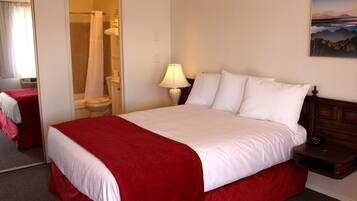 A hotel room with a large bed, a bedside table with a lamp, a bathroom with a shower curtain, and a painting on the wall.