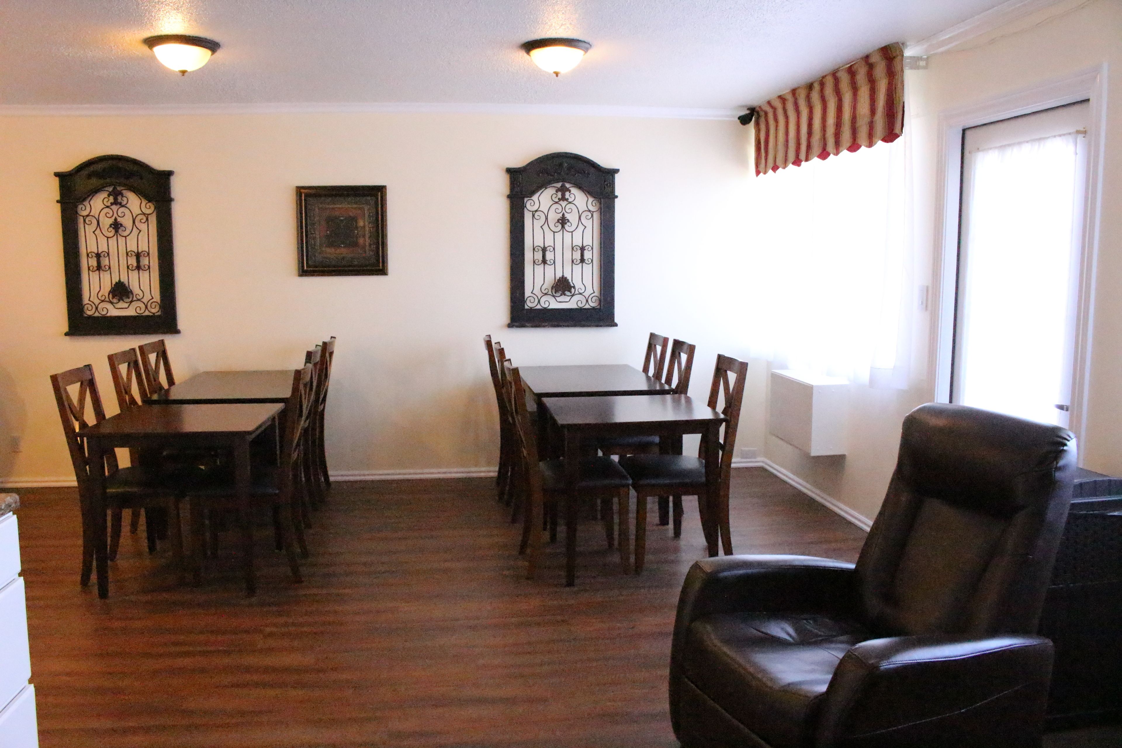 A dining room with a table and chairs, a leather chair, decorative wall sconces, and a window with a striped valance.