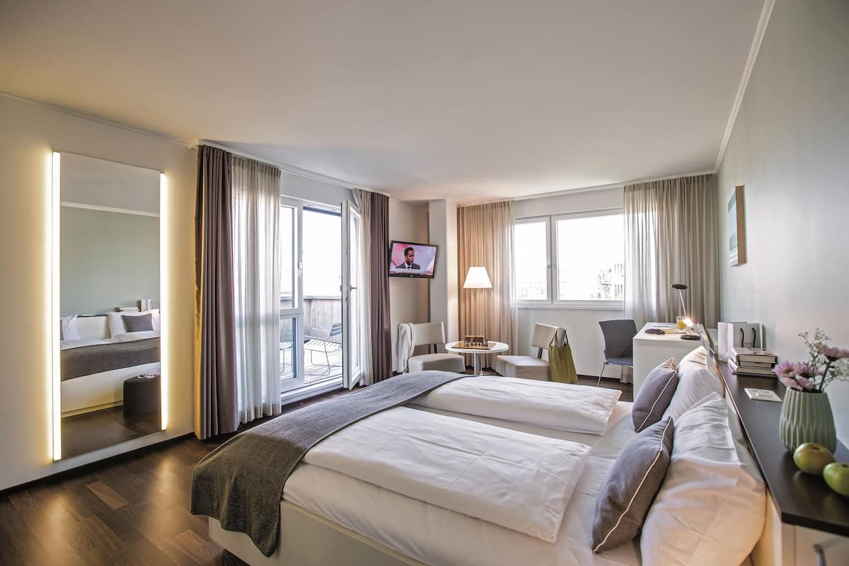 A hotel room with two beds, a desk, a chair, a TV, and a balcony with curtains.