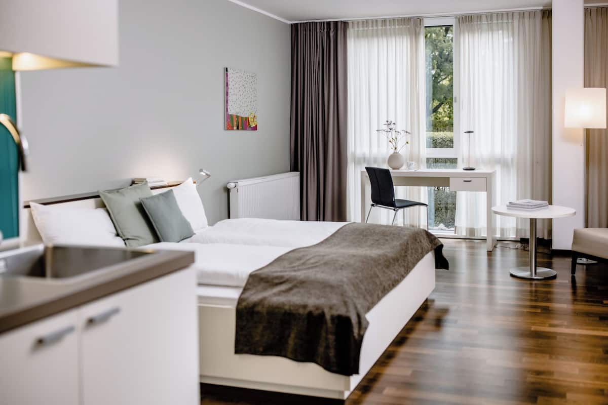 A modern hotel room with a bed, a desk, a chair, and a small table.