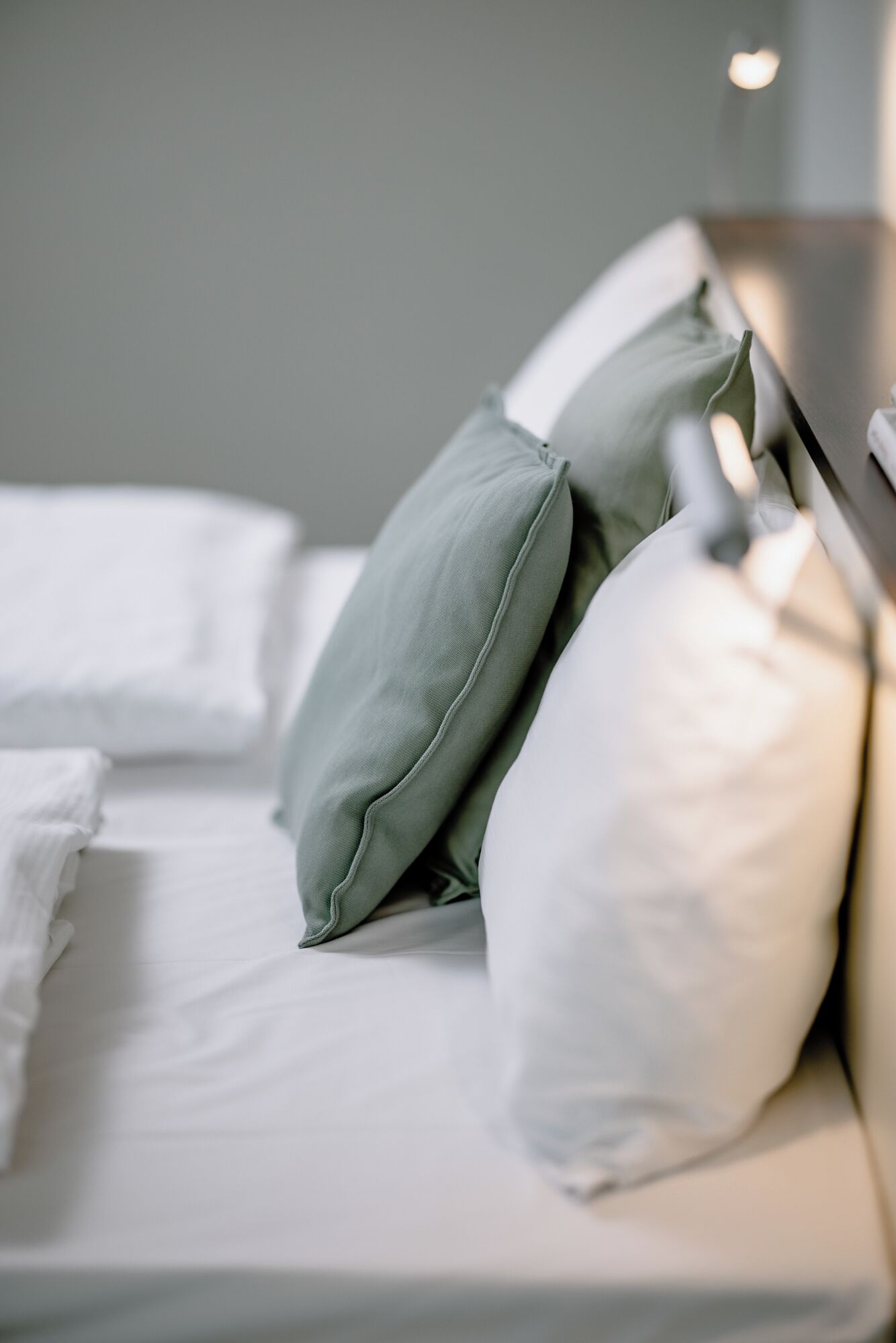 A bed with white linens and two pillows, one green and one white.