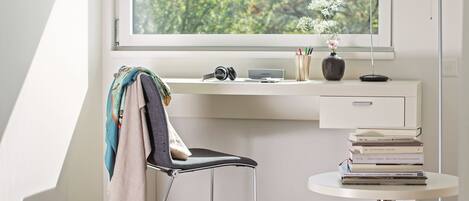 A modern office space with a desk, chair, and a round table with books. A window provides a view of greenery outside.