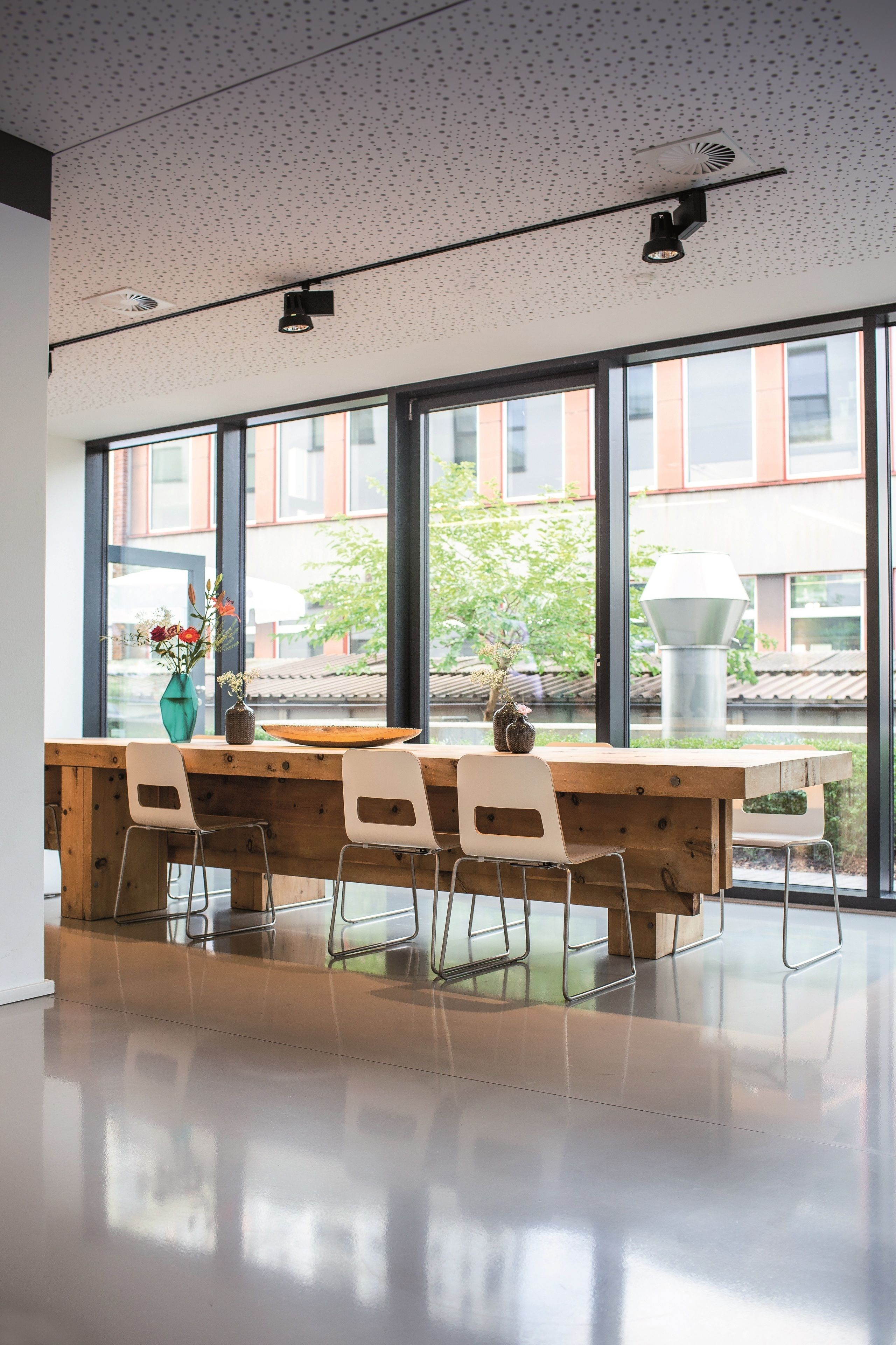 A modern interior with a wooden table and chairs, large windows, and a view of the outside.