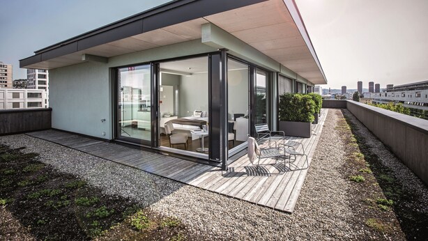 Una terraza moderna en la azotea con un área de estar cubierta de vidrio, mobiliario exterior y vistas al horizonte de la ciudad.