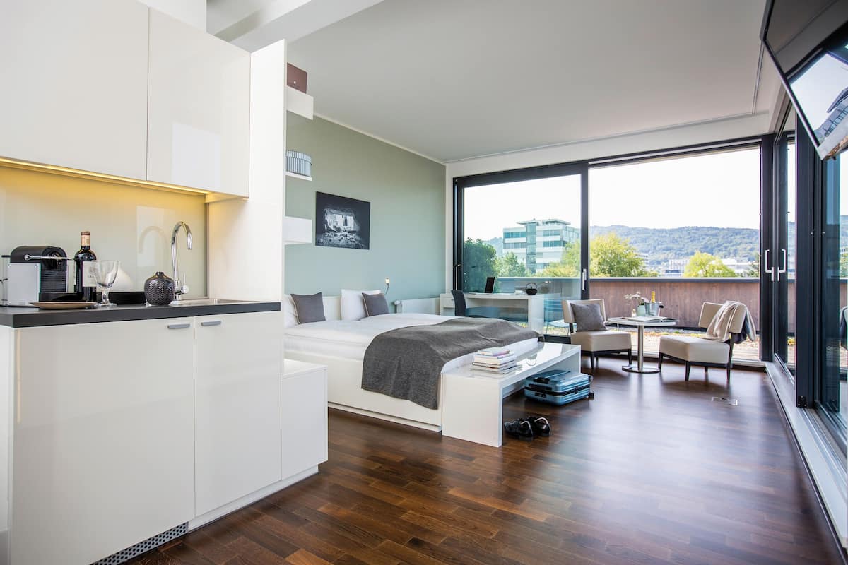 A modern bedroom with a large bed, a desk, and a balcony with a city view.