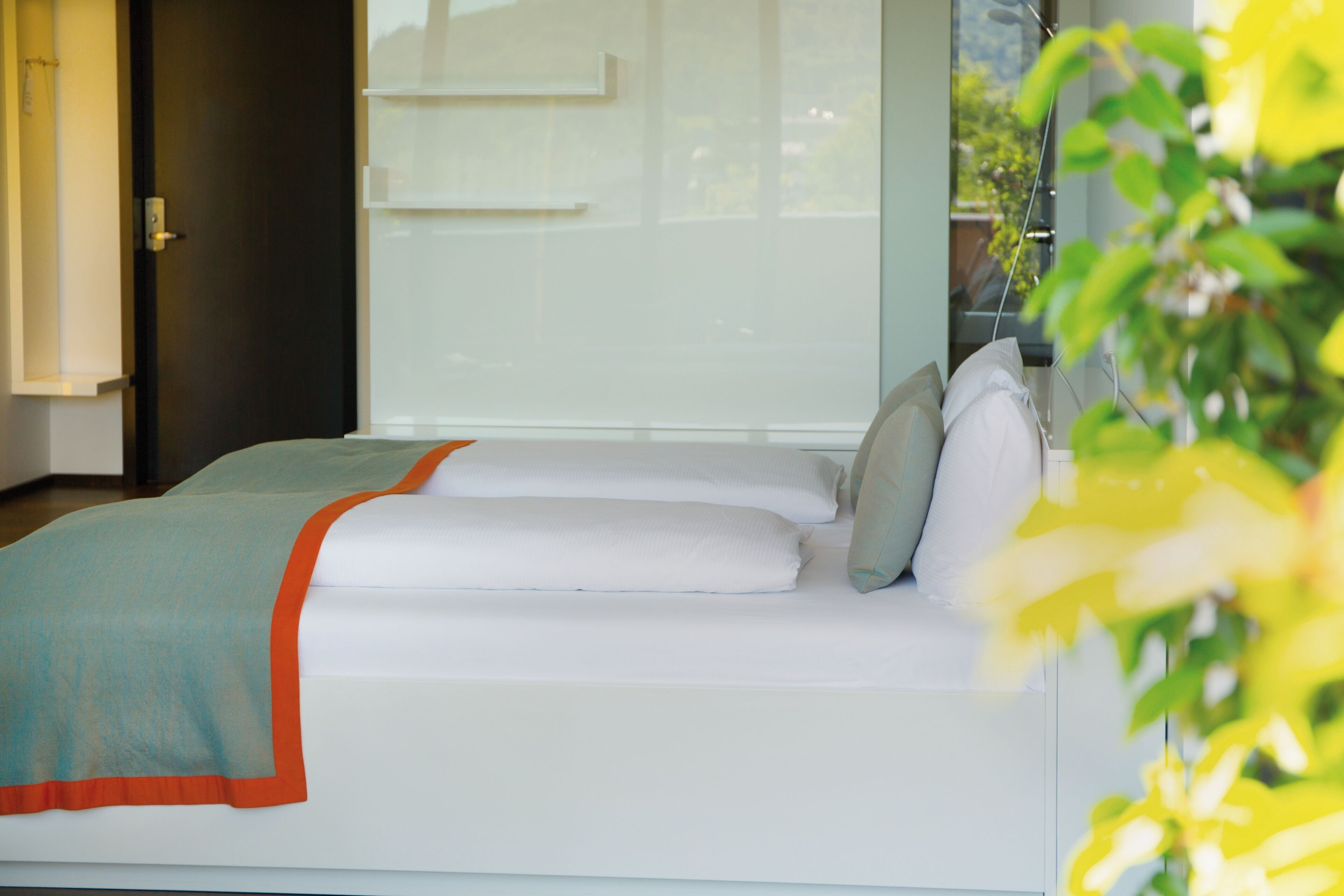 Ein modernes Zimmer mit Bett, Fenster und Pflanze.