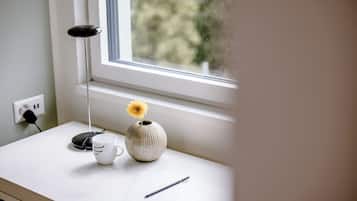 A desk with a vase containing a single flower, a cup, and a pen.