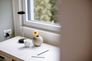 Uma mesa com um vaso contendo uma única flor, uma xícara e uma caneta.