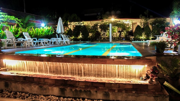 Piscina com cascata, rodeada por espreguiçadeiras e plantas em vasos.