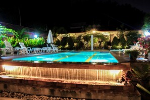 A swimming pool with a waterfall feature, surrounded by lounge chairs and potted plants. - Phuket Muay Thai House (Chalong)