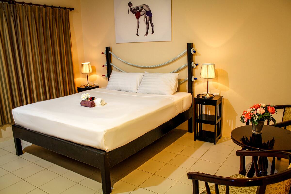 A neatly made bed with white linens, two bedside lamps, a small table with a vase of flowers, and a chair.