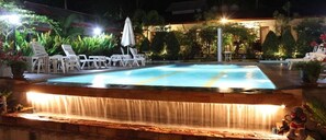 An outdoor swimming pool with a waterfall feature, surrounded by lounge chairs and potted plants. - Phuket Muay Thai House (Chalong)