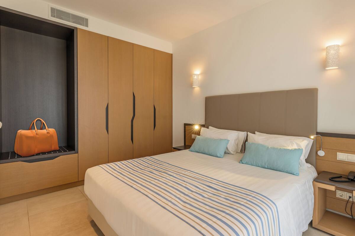 Une chambre d’hôtel avec un grand lit, une armoire, une table de chevet avec une lampe et un luminaire fixé au mur.