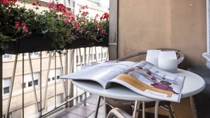 Un balcón con una mesa, una revista y flores rojas.