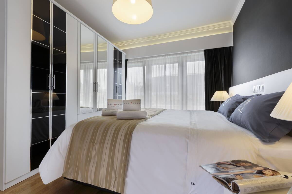A modern hotel room with a large bed, a wardrobe, and a magazine on the bed.