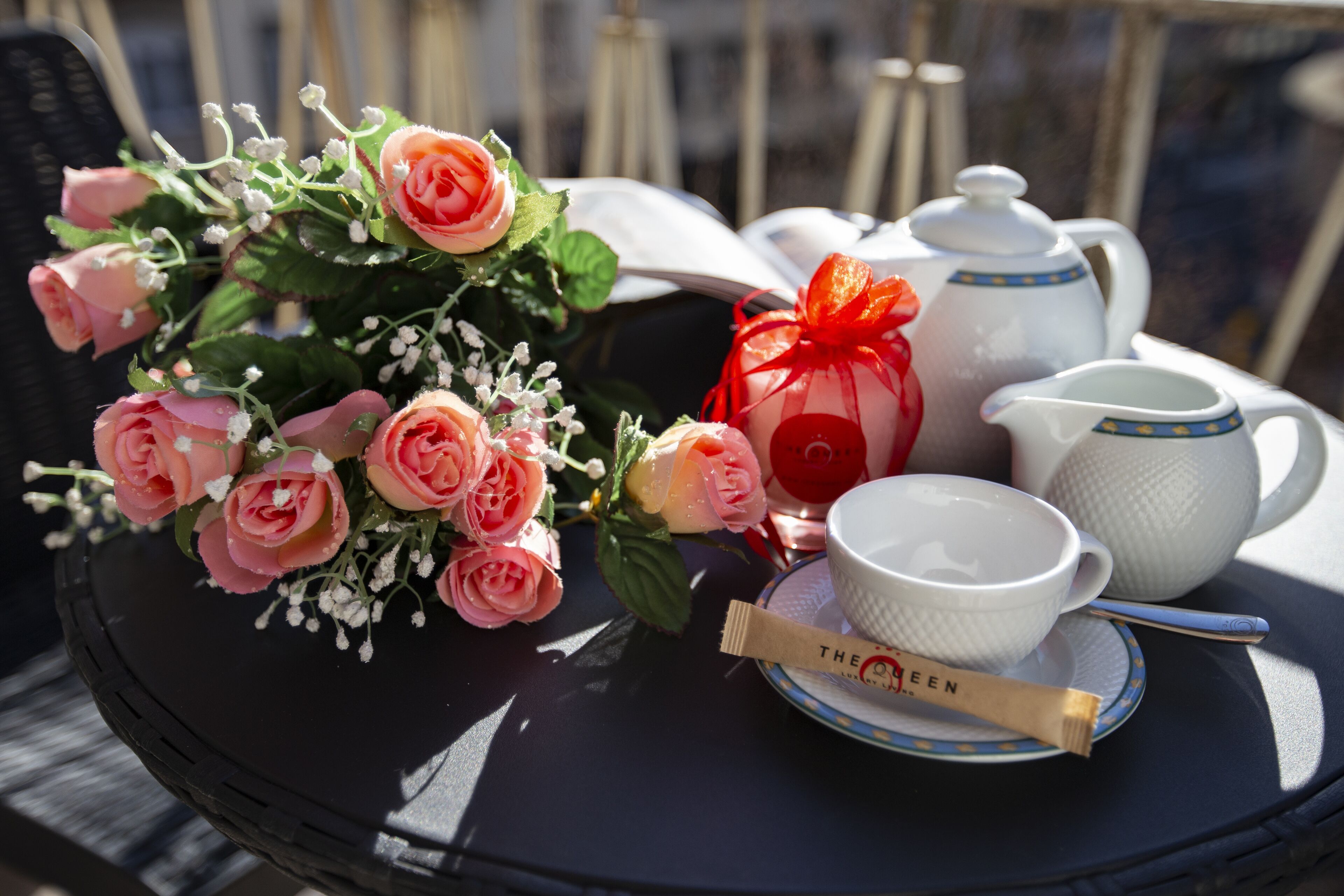 Een tafel met een bos roze rozen, een theepot, kopjes en een theedoos.