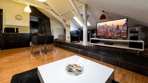 Un espacio de estar moderno con cocina, comedor y un televisor grande que muestra un paisaje urbano.