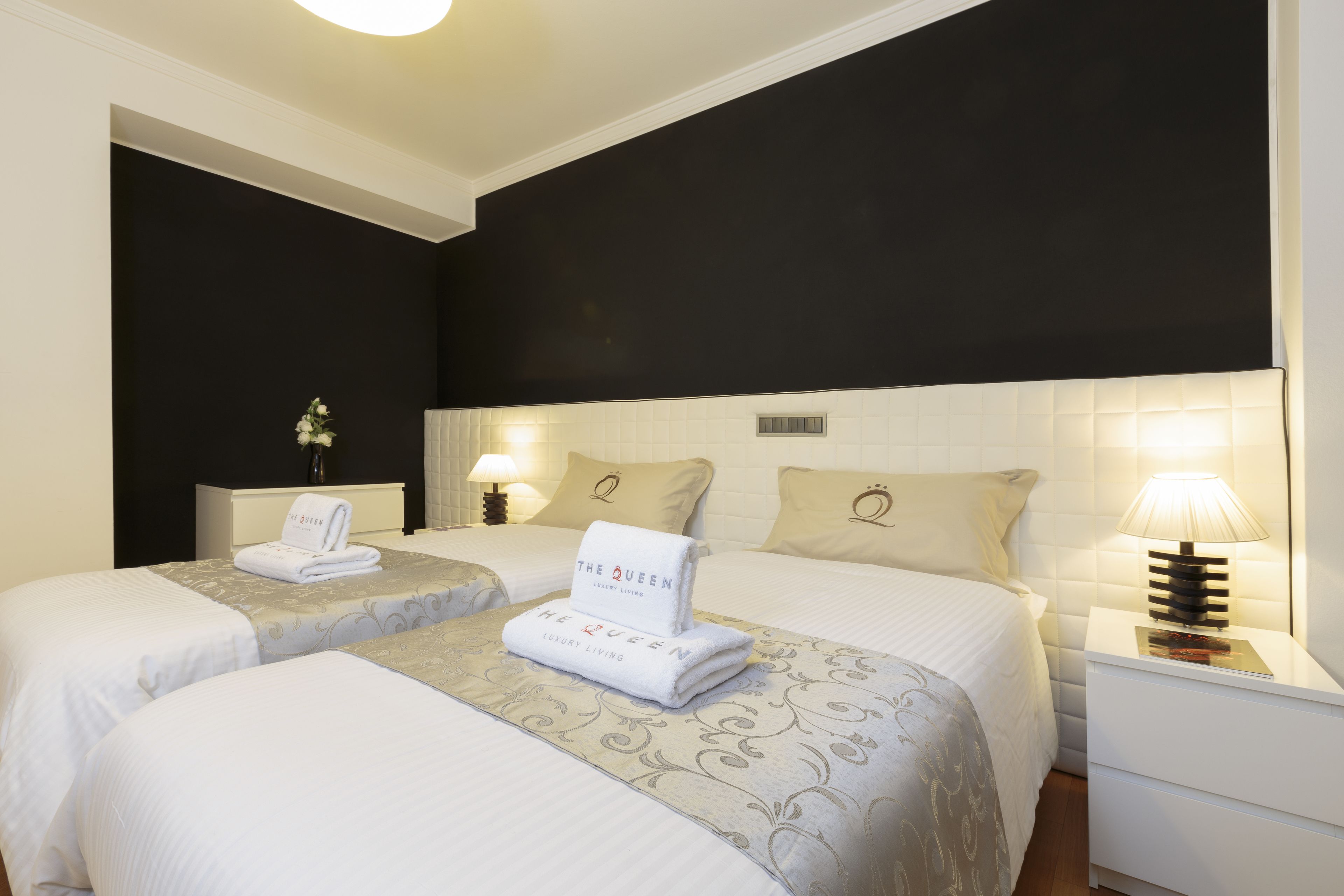 A hotel room with two beds, a nightstand with a lamp, and a wall-mounted light fixture.