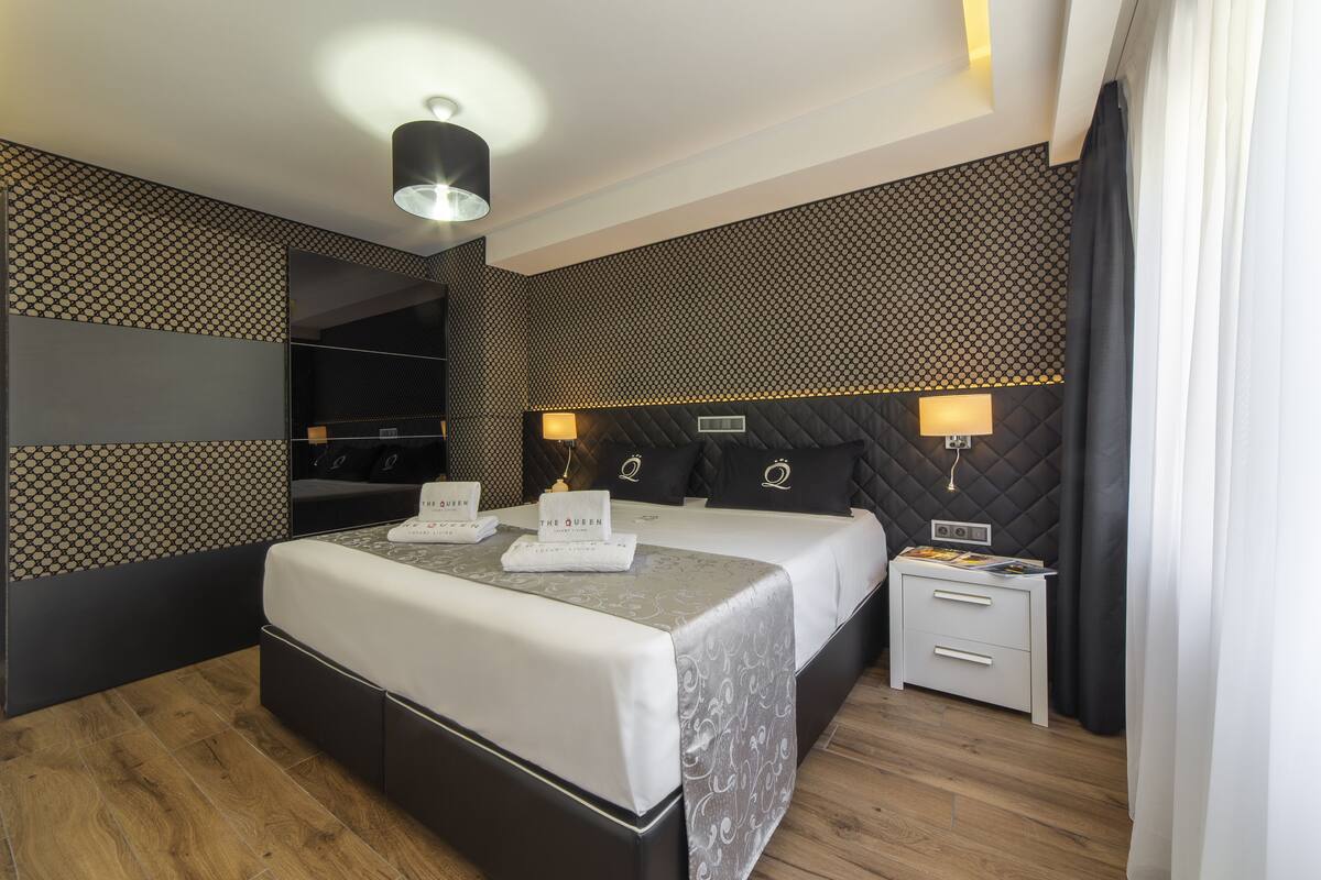 A modern hotel room with a large bed, a bedside table, and a mirror.