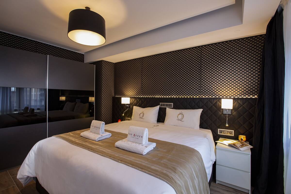A modern hotel room with a large bed, two bedside tables, a nightstand, a mirror, and a patterned wall.