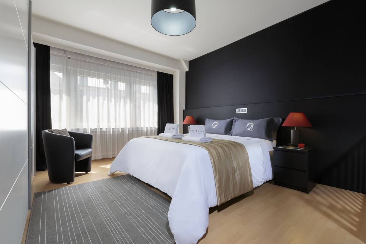 A modern hotel room with a large bed, a desk, and a chair.
