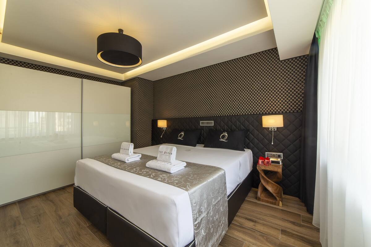 A hotel room with two beds, a modern design, and a small wooden side table with a lamp.