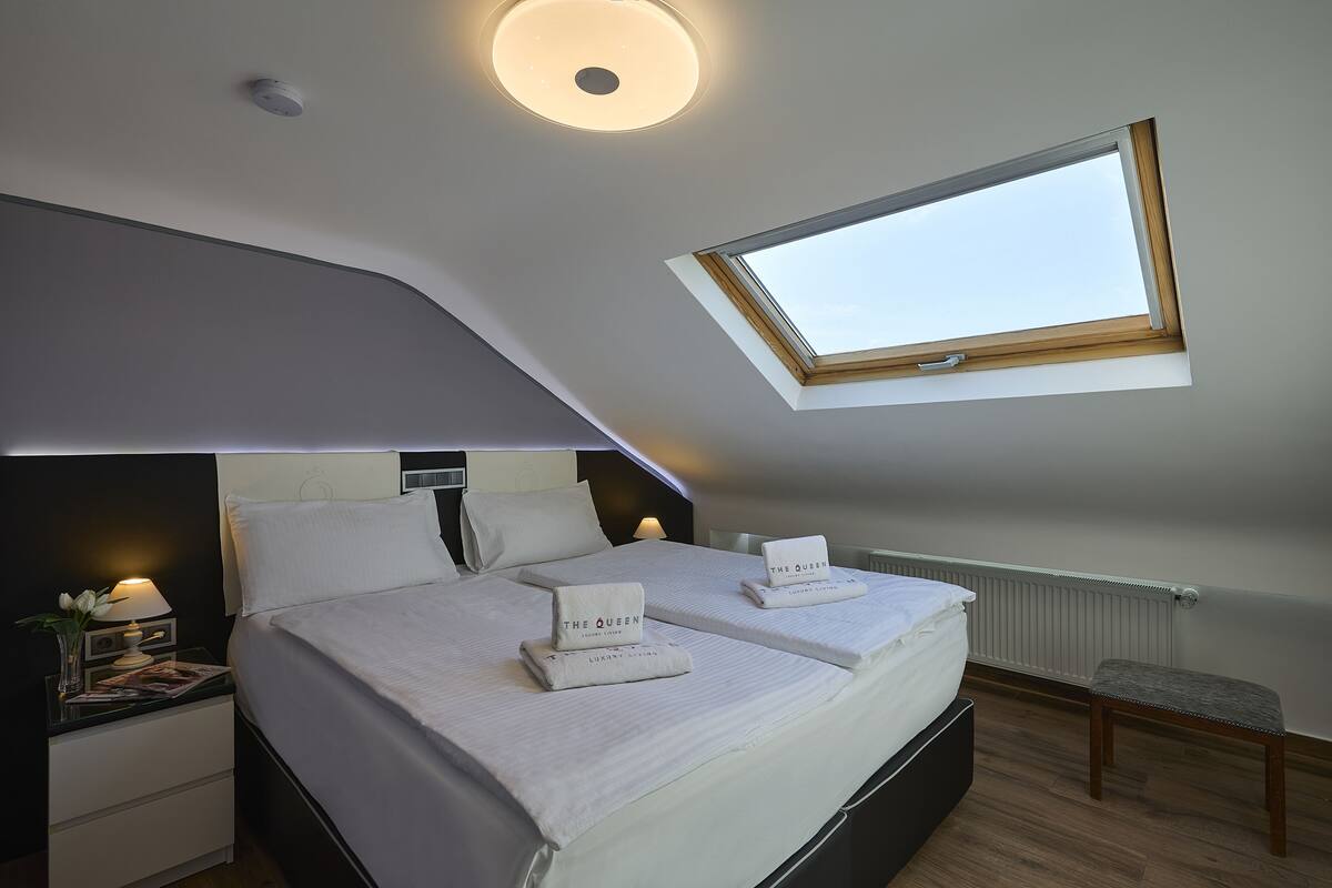 A bedroom with a skylight, two beds, a nightstand, and a small table with a lamp.