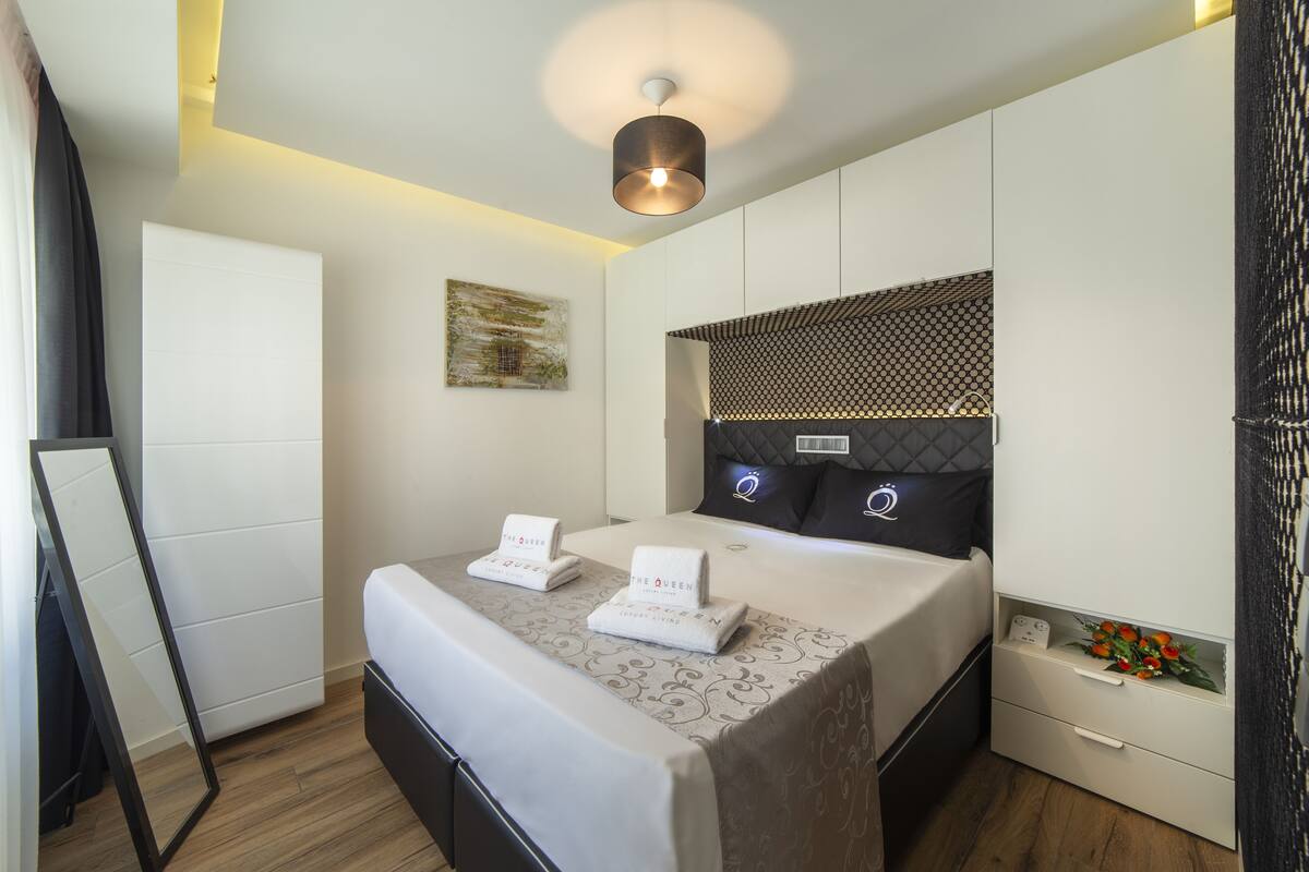 A modern hotel room with a neatly made bed, a bedside table with a vase of flowers, and a large mirror leaning against the wall.