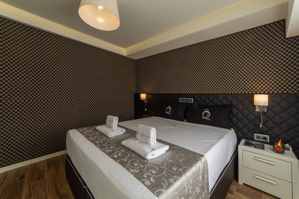 A hotel room with a large bed, two bedside tables, a nightstand with a lamp, and a patterned wall.