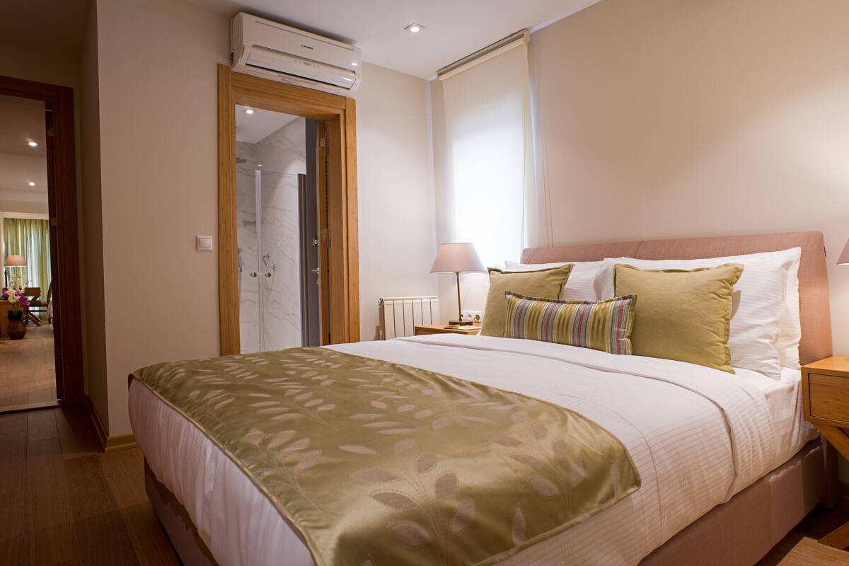 Una habitación de hotel con una cama, lámparas de noche, una mesita de noche y un equipo de aire acondicionado.