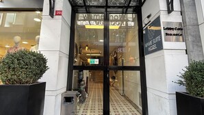 The entrance to Wame Hotel with a black metal gate, a doormat with the hotel's logo, and a sign indicating the lobby cafe and brasserie. - Wame Suite Hotel (Istanbul)