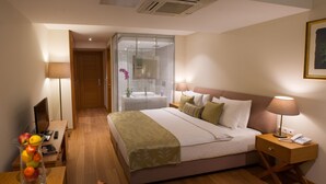 A hotel room with a bed, bedside lamps, a desk with a computer, a vase of fruit, and a window with blinds. - Wame Suite Hotel (Istanbul)