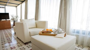 A modern hotel room with a white sofa, a matching ottoman, and a breakfast tray with orange juice and tea. - Wame Suite Hotel (Istanbul)