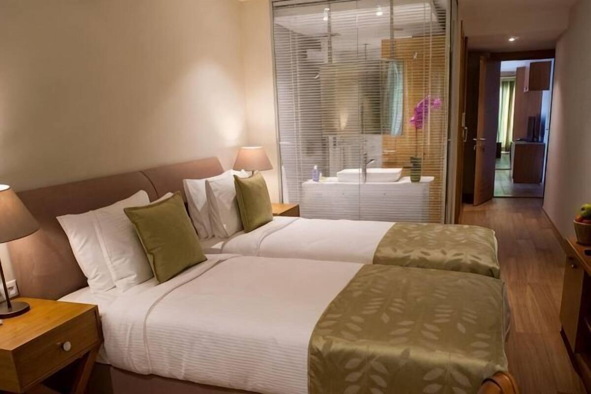 Habitación de hotel con dos camas, baño con espejo y pasillo que da a otras habitaciones.